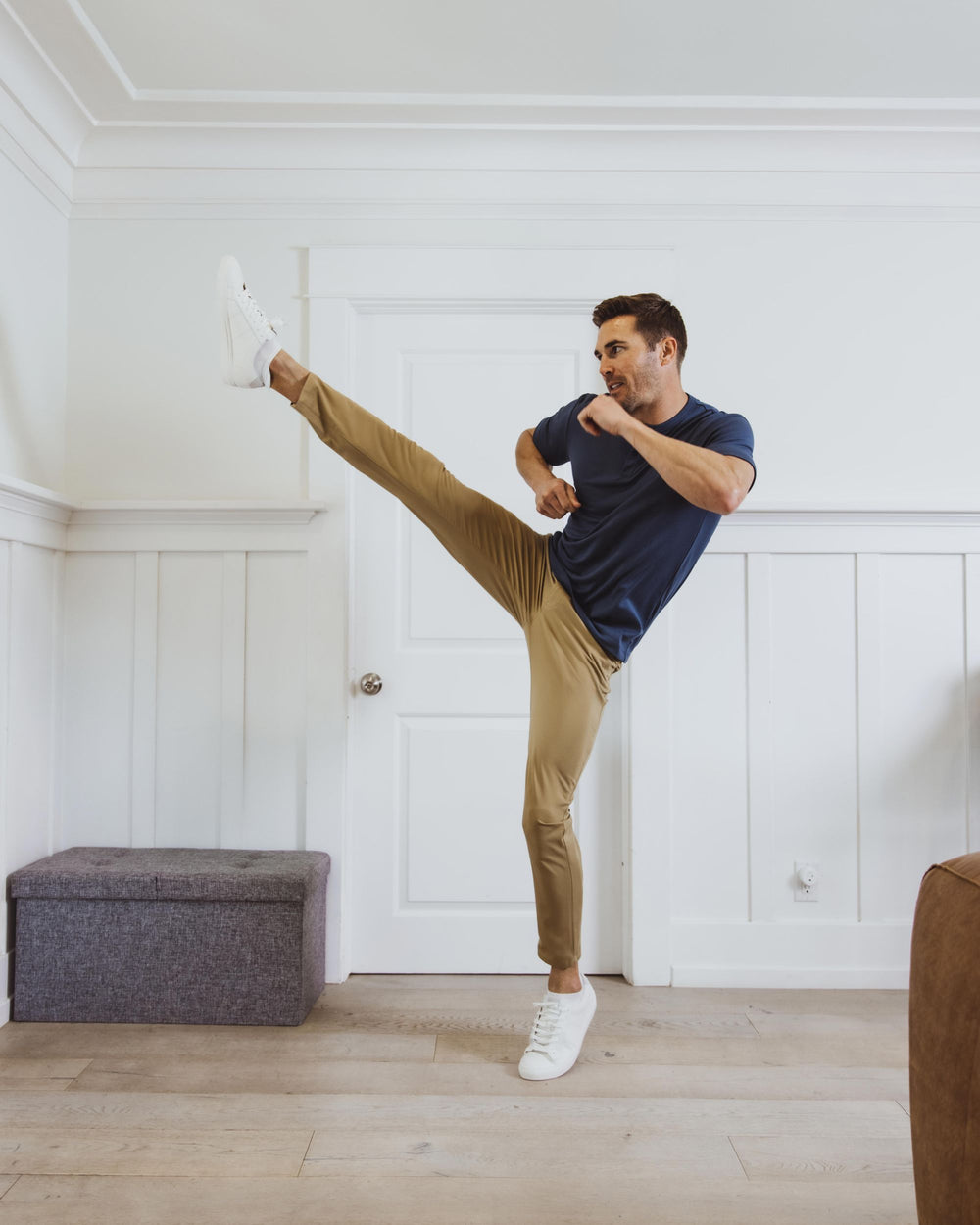 Man performing a high kick in a room with white walls and wooden flooring.
