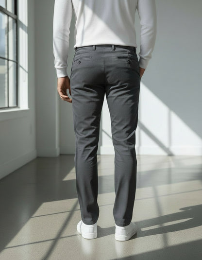 Person wearing gray pants and a light gray sweater in a bright room with large windows.