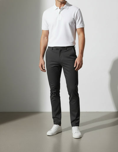 Man wearing a white polo shirt and black pants standing against a plain background