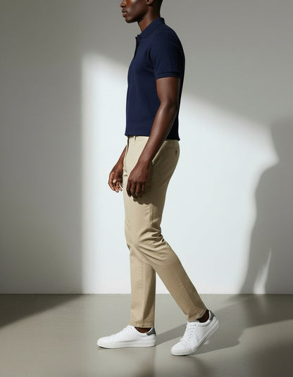 Man wearing a navy polo shirt, beige pants, and white sneakers against a neutral background